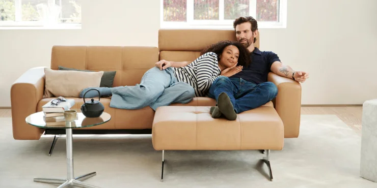 Couple lounging on modern camel-colored leather sofa with minimalistic metal legs in bright airy room