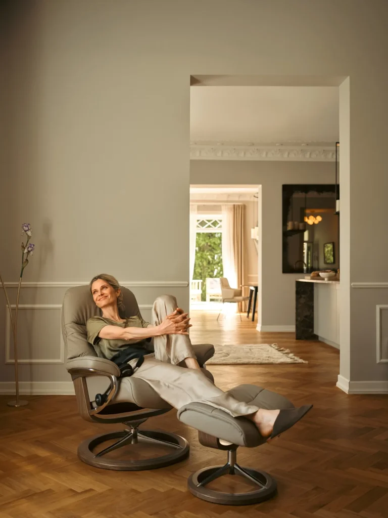 Woman smiling in Stressless Sunrise recliner with smoked oak ottoman