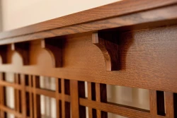 Close-up of Arts and Crafts style wooden corbel brackets supporting a horizontal beam above latticed headboard detail showing rich quartersawn oak grain pattern