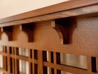 Close-up of Arts and Crafts style wooden corbel brackets supporting a horizontal beam above latticed headboard detail showing rich quartersawn oak grain pattern