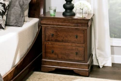 Nightstand in rich brown featuring two drawers with decorative pulls stepped crown molding and traditional bracket details styled with glass accessories