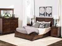 Traditional Louis Philippe bedroom set in dark cherry featuring sleigh bed dresser with mirror and nightstands accented by black lamps and botanical artwork