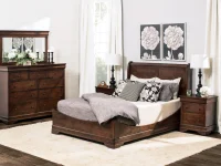 Traditional Louis Philippe bedroom set in dark cherry featuring sleigh bed dresser with mirror and nightstands accented by black lamps and botanical artwork