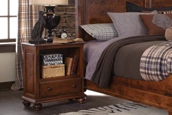 Traditional bun foot nightstand in distressed cherry featuring open shelf storage drawer turned legs styled with dog lamp plaid bedding and rustic decor