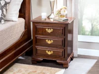 Traditional three-drawer nightstand in dark cherry wood featuring brass chippendale pulls decorative bracket feet and styled with silver vase fresh flowers