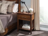 Transitional Shaker nightstand in brown maple featuring single drawer chrome pull open shelf tapered legs styled with industrial task lamp and white hydrangeas