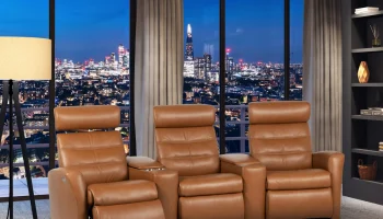 Tan leather three-seat H2 Seating power reclining sofa with tufted backrests, plush armrests, and built-in footrests, featuring two central consoles with cup holders and storage