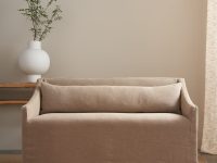 Rowe - A minimalist living room featuring a beige sofa with a cushioned backrest, placed on a textured beige rug