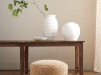 Rowe - Close-up view of a beige shaggy ottoman under a wooden console table, adorned with white textured vases and a branch with green leaves