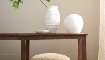 Rowe - Close-up view of a beige shaggy ottoman under a wooden console table, adorned with white textured vases and a branch with green leaves