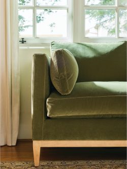 Rowe - Close-up view of a green velvet sofa with plush cushions, featuring visible stitching and wooden legs