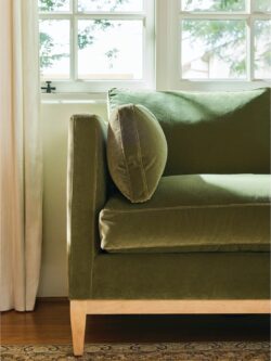 Rowe - Close-up view of a green velvet sofa with plush cushions, featuring visible stitching and wooden legs