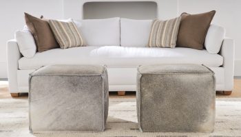 Rowe - Two Grey Cowhide Ottomans In Front Of White Sofa With Brown And Striped Pillows Home Decor