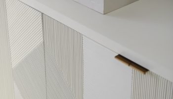 Rowe - White console table with geometric ribbed panel doors, topped with a white bowl and a book