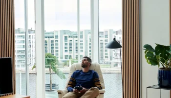 Man relaxing in vanilla walnut Stressless Max recliner by city window