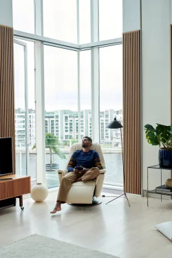 Man relaxing in vanilla walnut Stressless Max recliner by city window