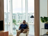 Man relaxing in vanilla walnut Stressless Max recliner by city window